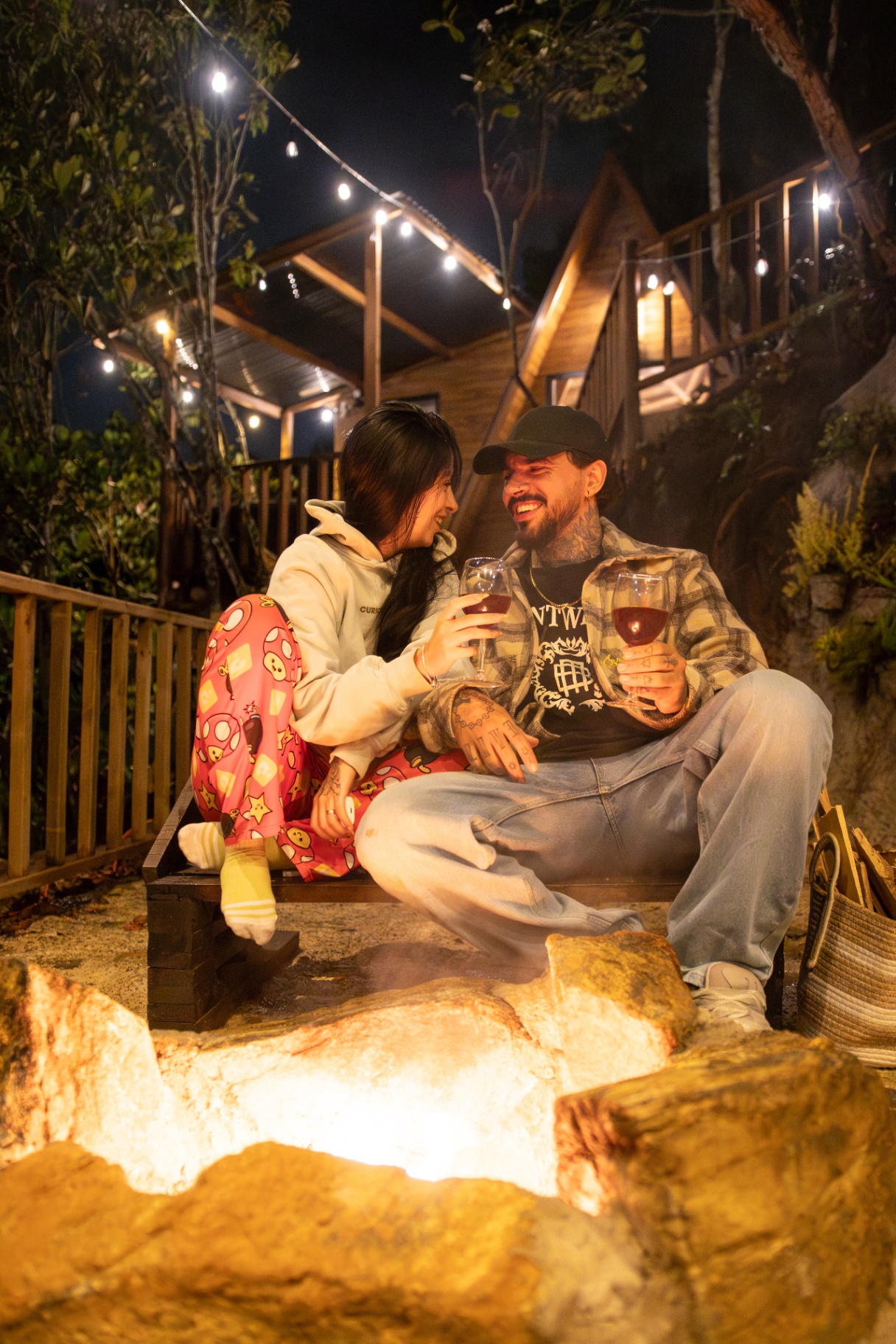 Pareja brindando con copas de vino frente a un chalet iluminado por luces cálidas en Santa Elena